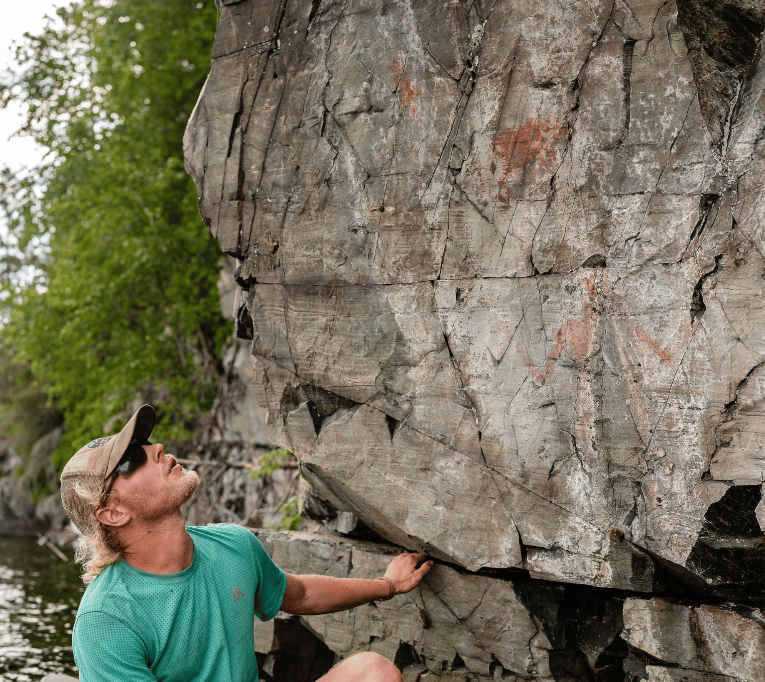 A traveler examining the ancient markings on a rock wall in Temagami, Ontario, exploring the region's rich cultural and historical heritage, featured in Karibu Adventures' outdoor and cultural tours, offering an immersive experience into the area's Indigenous history.