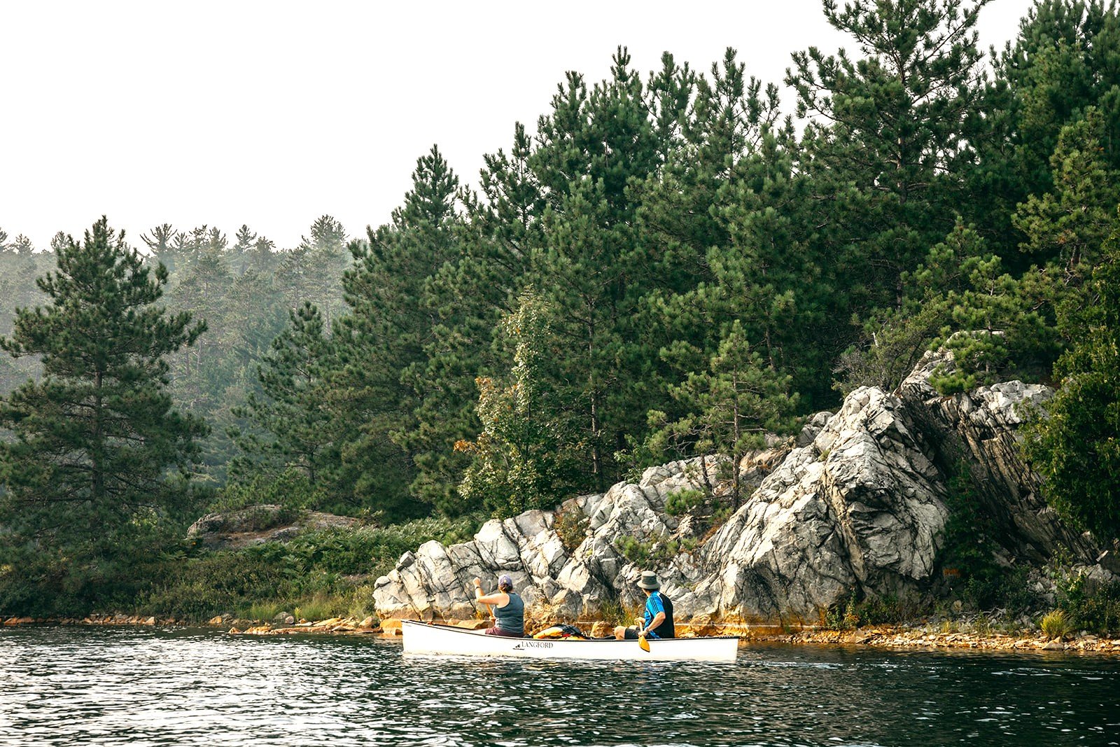 Two travelers canoeing on the serene waters of Wolf Lake, surrounded by lush forests and rugged landscapes, capturing the adventure and natural beauty of Karibu Adventures' Ontario canoe trips, including the iconic Temagami region and its best canoe routes.